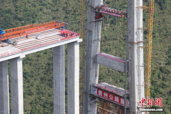 11月22日，峰林特大橋4號(hào)主塔中橫梁正在吊裝。當(dāng)日，隨著1470噸裝配化預(yù)制中橫梁提升到位，貴州省黔西南布依族苗族自治州興義環(huán)城高速公路峰林特大橋4號(hào)主塔中橫梁成功吊裝，由此刷新了山區(qū)峽谷橋梁預(yù)制吊裝混凝土構(gòu)件重量世界記錄。峰林特大橋是屬全線控制性工程。大橋跨越馬嶺河峽谷，全長(zhǎng)1163米，主跨采用550米懸索橋，橋面離谷底364.2米，是中國(guó)山區(qū)第一座大跨徑鋼混疊合梁懸索橋。中新社記者 瞿宏倫 攝
